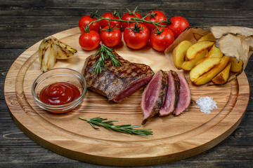 Grilled sliced beef steak with rosemary and tomatoes, on a wooden table