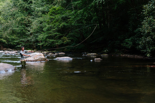 Man casting and fly-fishing in clear river trying to catch fish