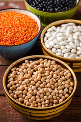 Fototapeta premium Assorted beans in bowls with red lentil, chick-pea and kidney bean on wooden background.