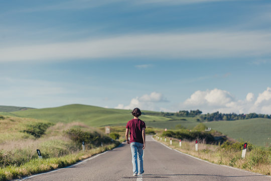 Back view of a teenage boy walking a long road through the fields in Italy