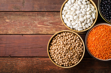 Assorted beans in bowls with red lentil, chick-pea and kidney bean on wooden background.