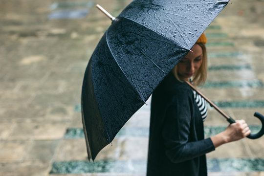 Side view of a woman holding an umbrella in a rainy day.