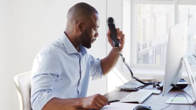 Young black man using phone and computer in office, close up