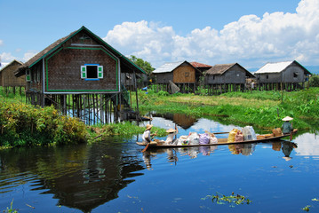 Fototapeta na wymiar Locals transporting goods on a small boat through a floating village on the Inle lake, Myanmar.
