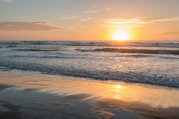 Rising Sun Reflecting on Wet Sand with Calm Ocean Waves in the Background