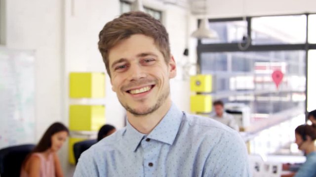 Young white man in office walks into focus, and smiles