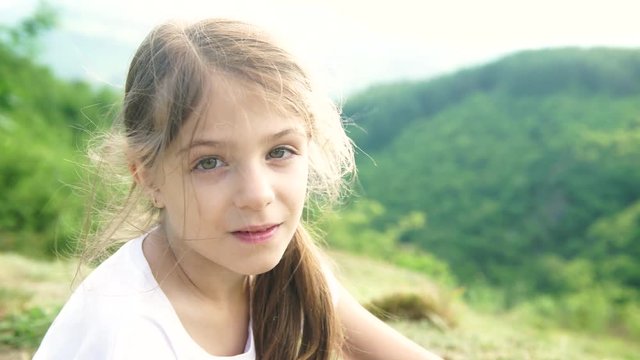Cute female kid portrait on top of the hill with a green landscape behind her, 4K