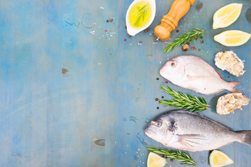 fresh sea fish set - dorada breams with lemon, herbs and spices on blue wooden background