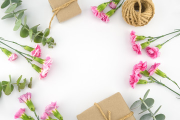 Brown gift boxes and ropes decorated with baby eucalyptus leaves and pink carnation flowers on white background with copy space