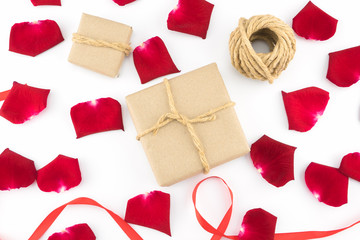 Brown gift boxes, ropes and red ribbon decorated with red rose petals on white background