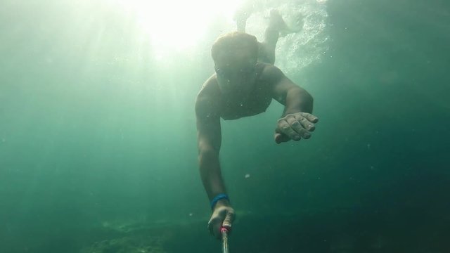 Caucasian swimmer male dives iinto the sea depths under water in glare of sunlight at tourist resort. Active rest and healthy lifestyle, water sports in holiday. Underwater slow motion
