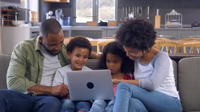Family Sitting On Sofa In Open Plan Lounge Using Laptop