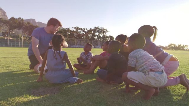 Young school kids and teacher sitting with ball in field