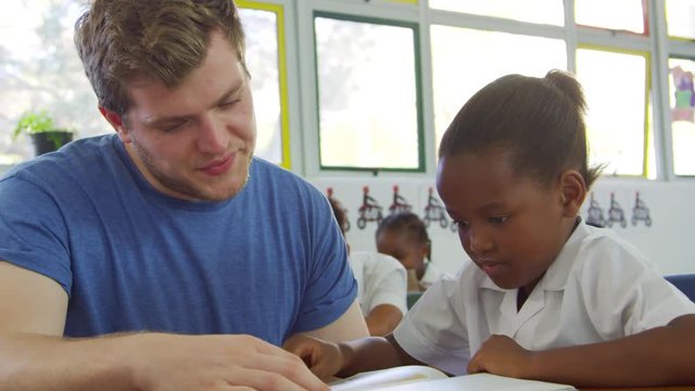 Volunteer teacher helping schoolgirl at her desk, close up