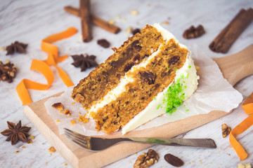 Close up of a homemade carrot cake with raisins, walnuts and cinnamon over white wooden background. Cream cheese frosting.