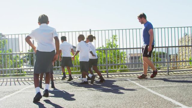 Teacher plays football with young kids in school playground
