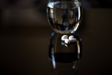 Pills and water glass on shiny surface