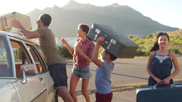 Family Loading Luggage Onto Car Roof Rack Ready For Road Trip