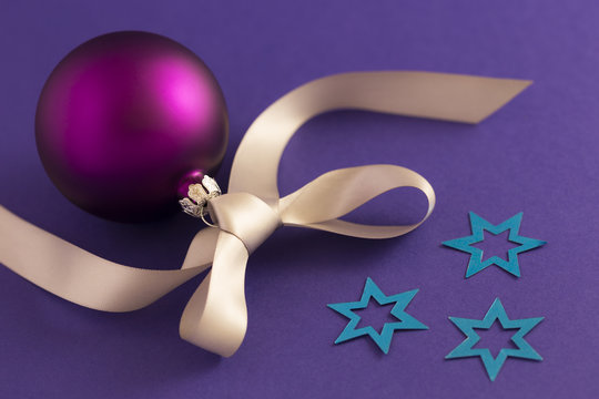 Beautiful purple christmas ball with satin effect, grey gift ribbon and metallic blue stars on purple background.