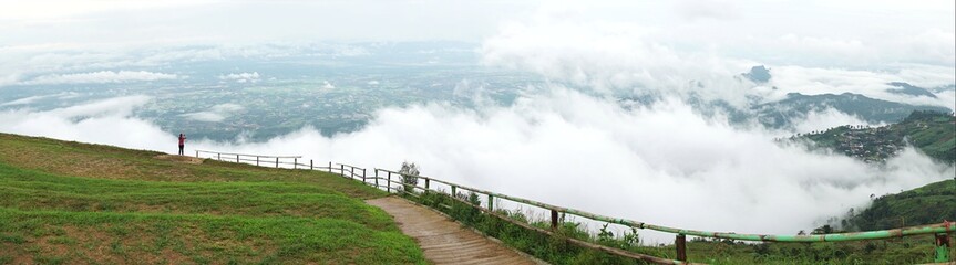Panorama of woman looking at view of mountain landscape with waves of  fog and cloudy sky. Phu Tub Berg, Phetchabun province, Thailand