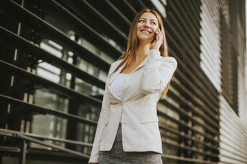 Fototapeta premium Pretty businesswoman with mobile phone in front of office building