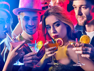 Cocktail party with group people dancing and drink cocktail. Women and men have fun in night club. Happy girl with alcohol drink on foreground. Opening of a new strip club.