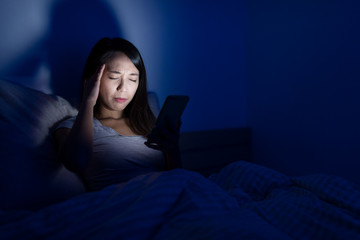 Woman using cellphone and feeling headache on bed