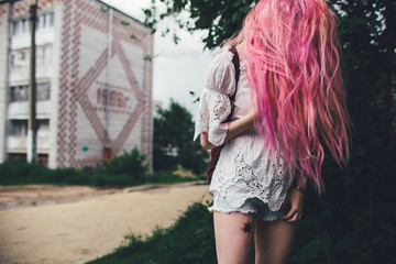 The beautiful girl with pink hair walks on the city street in the summer