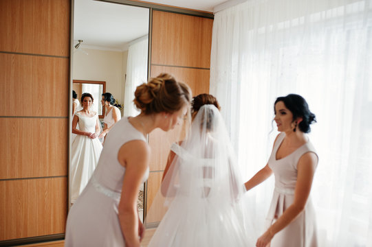 Bridesmaids helping gorgeous bride to dress up and get ready for her wedding ceremony.