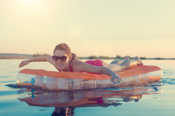 Young smiling woman in sunglasses rowing on the mattress in water