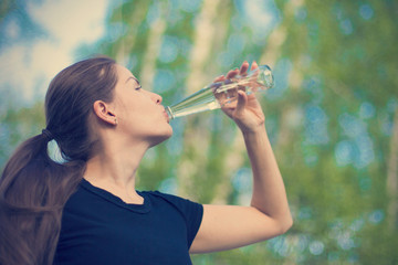 Young woman drinks from a glass bottle of fresh water close up