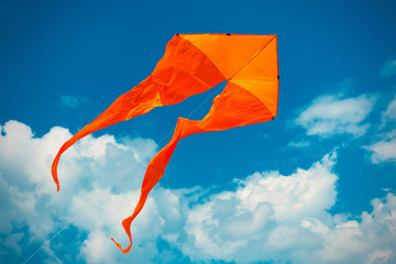 Orange kite in the blue sky with white clouds