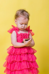 Girl toddler in a pink dress on a yellow background holding a smartphone