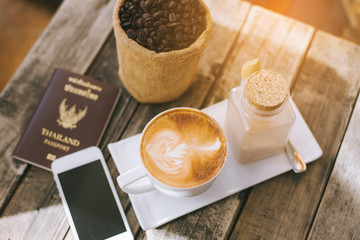 Cup of hot coffee with the telephone placed on a wooden table.