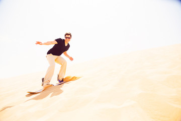 Fototapeta na wymiar Tourist Sandboarding In The Desert
