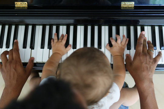 Toddler learning to play piano with father