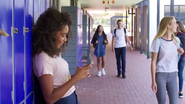 Girl using phone and boy using locker in school corridor
