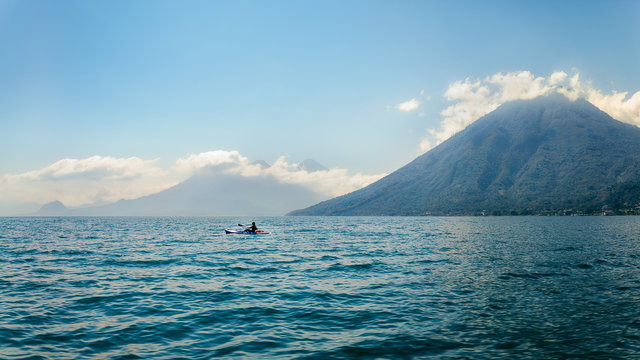 A Kayaker in the blue waters of Lake Atitlan in Guatemala, on a misty morning in front of volcano San Pedro. Further away in the mist we can see Volcanos Toliman and Atitlan.