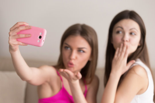 Close up image of mobile phone in girls hand taking selfie photo, sending air kisses to camera on blurred background. Young women recording video message or greeting, sharing pictures in social media