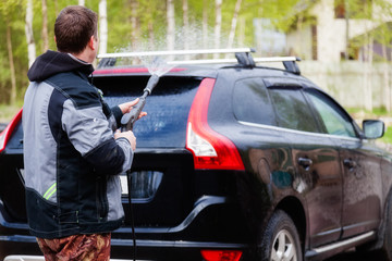 A man washes his car in the yard