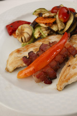 Chicken with bacon and grilled vegetables arranged on a plate, Traditional dish in elegant setting, Selective focus with soft light