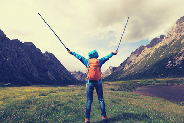 cheering young backpacking woman hiking in mountains