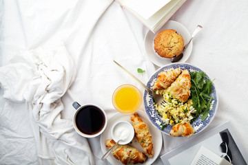 Breakfast in bed. Scrambled eggs with cheese croissants, raspberry muffin and black coffee. Lazy morning concept. Flat lay with copy space.