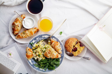 Breakfast in bed. Scrambled eggs with cheese croissants, raspberry muffin and black coffee. Lazy morning concept. Flat lay with copy space.