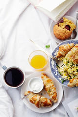 Breakfast in bed. Scrambled eggs with cheese croissants, raspberry muffin and black coffee. Morning treat concept. Composition with copy space.