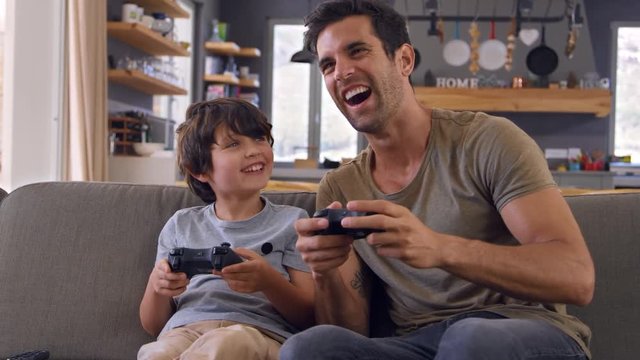 Father And Son Sitting On Sofa In Lounge Playing Video Game