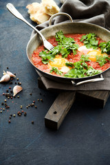 Shakshuka fried eggs with tomatoes, onions and spices in frying pan on a dark blue cracked background  
