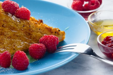 French toast close up, meal served on blue plate with raspberries and bowls of honey and jam
