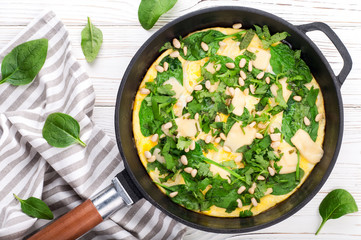 Spinach tortilla in pan on white background. Omelet with eggs, spinach, pine nuts and vegetables. Delicious breakfast or appetizer snack. Top view