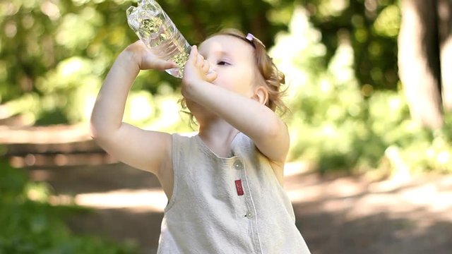 Charming funny happy child is drinking water from a bottle in the summer.